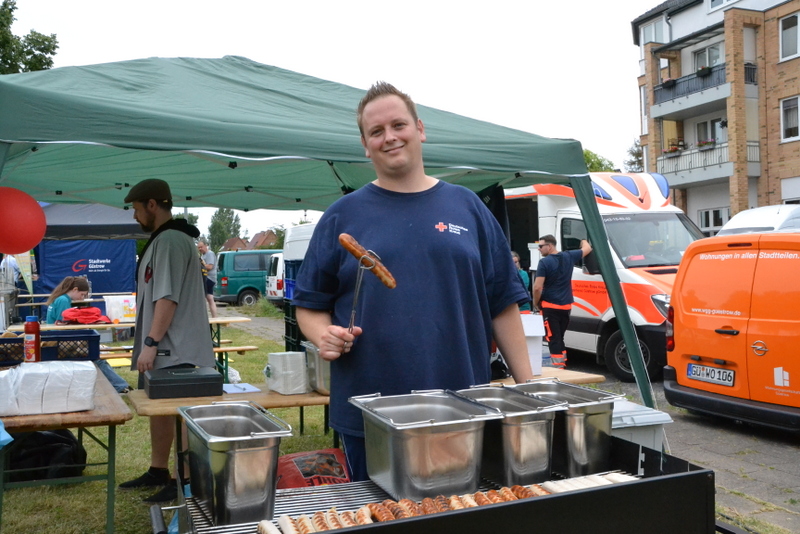 Bild zeigt Herrn Christopher Pusch am Grillstand mit einer Bratwurst in der Grillzange