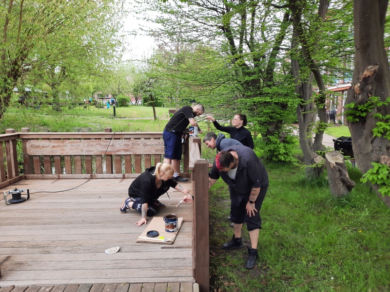 Bild zeigt einen Mitarbeiter des Pflegeheimes beim abschleifen des Holzsteges und 4 andere Mitarbeitende beim neu aufbringen der Schutzlasur