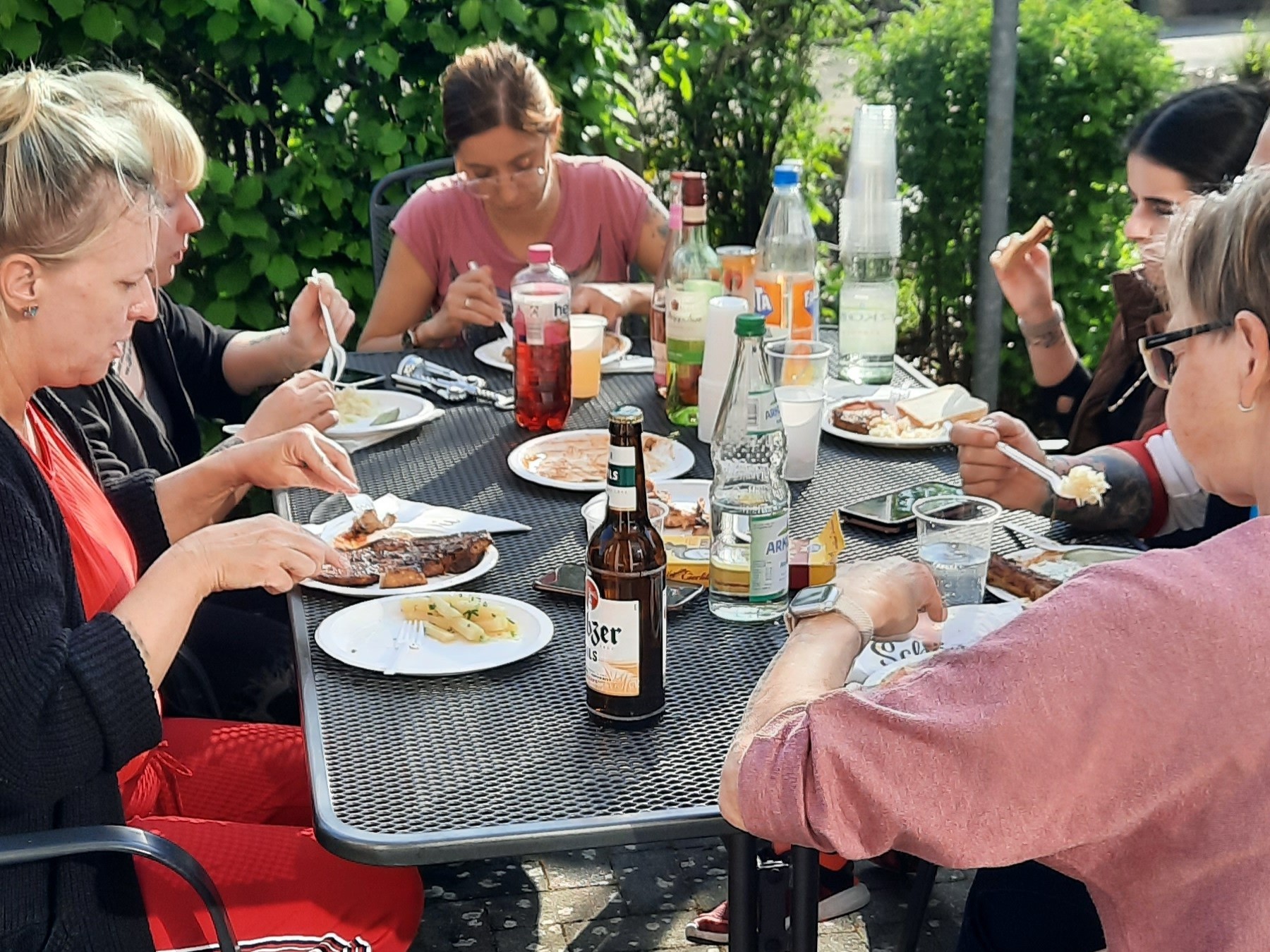 Bild zeigt die Mitarbeitenden gemütlich am Tisch sitzend und den Grillabend genießen nach der getanen Arbeit