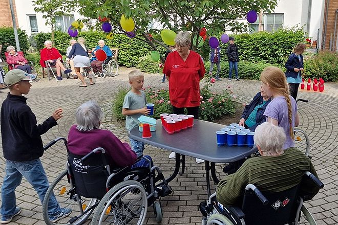Bild zeigt einige Kinder und Senioren im Rollstuhl bei einem Ping-Pong-Becher Spiel an einem Tisch der im Freien aufgestellt ist